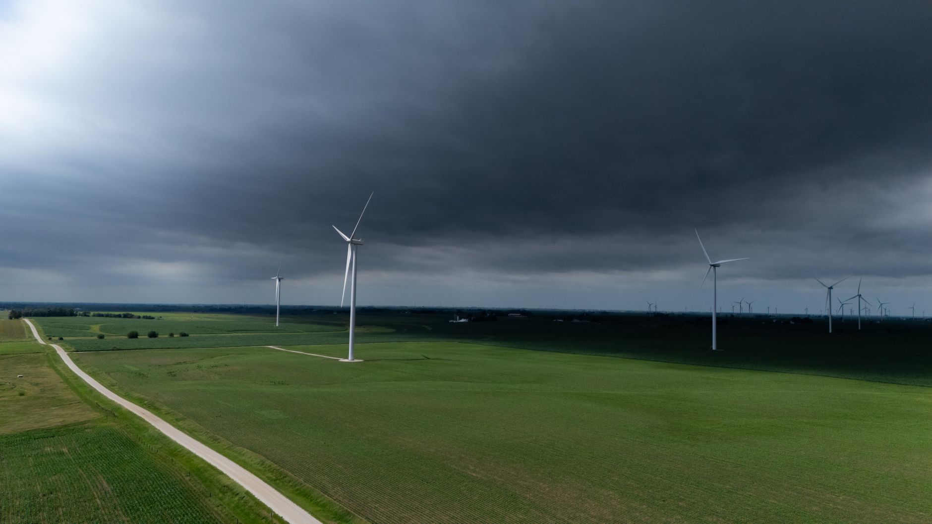 Vindmøller over en grøn mark under en mørk himmel